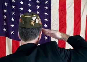 A Veteran wearing a decorated cap, saluting the American Flag